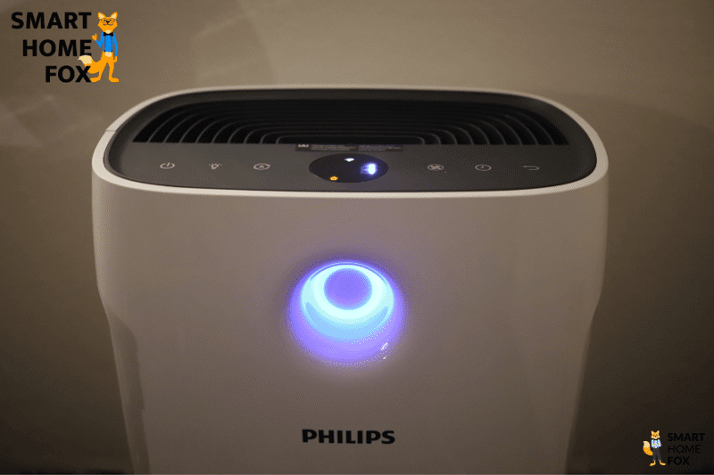 Очиститель воздуха Philips Series 2000i AC2889/10 стоит на столе, светодиодное цветовое кольцо светится синим цветом.